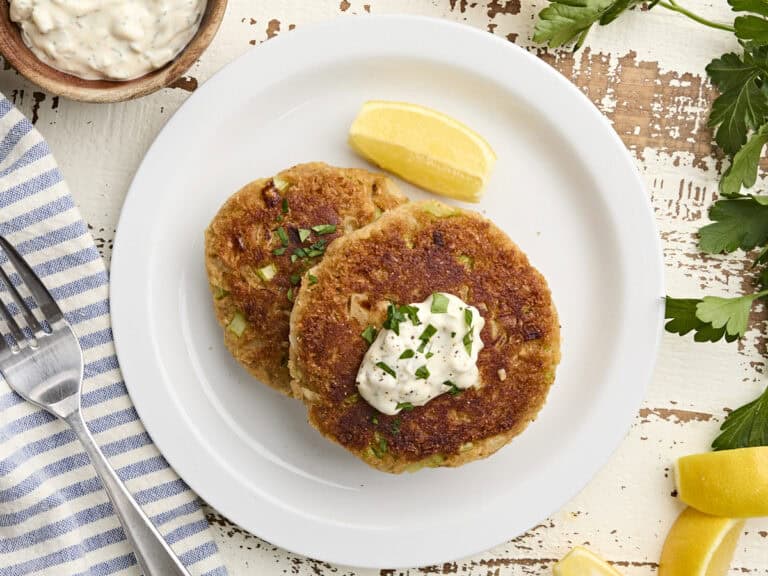 Overhead view of two homemade crab cakes on a plate with a lemon wedge and tartar sauce.