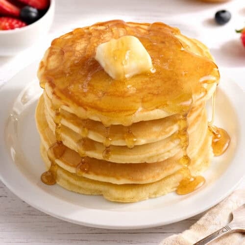 Side view of a stack of homemade pancakes with butter and syrup.