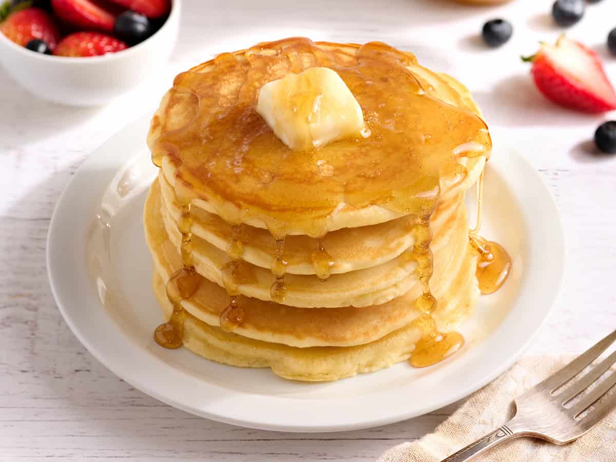 Side view of a stack of homemade pancakes with butter and syrup.