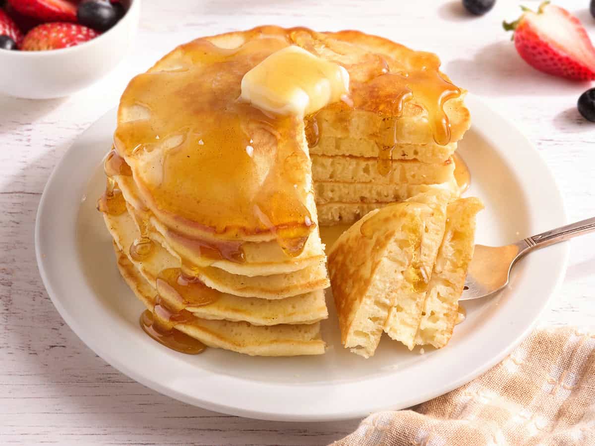 Side view of a stack of homemade pancakes with butter and syrup, with a quarter cut out of the stack and pieces of pancake on a fork.