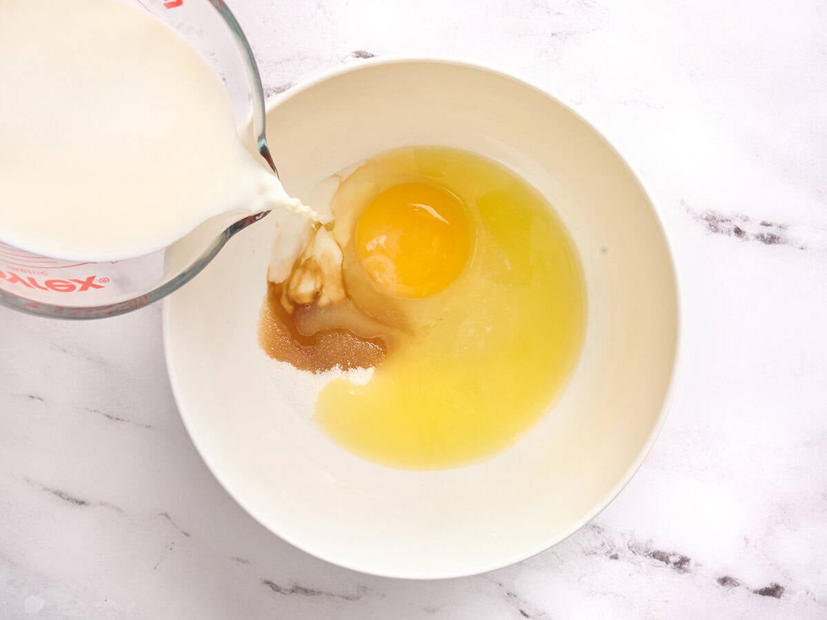 Egg, melted butter and sugar in a bowl with milk being poured in.