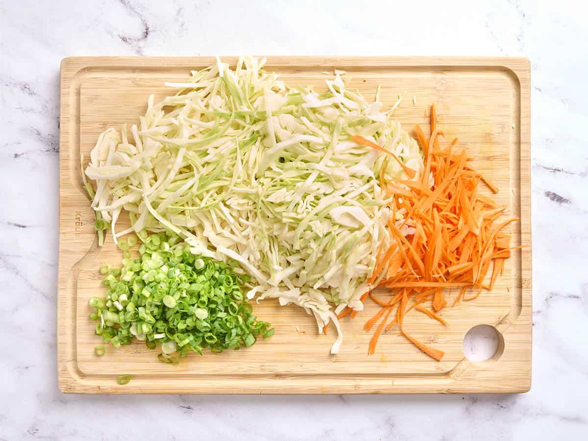 Shredded cabbage, carrots, and sliced green onions on a cutting board.