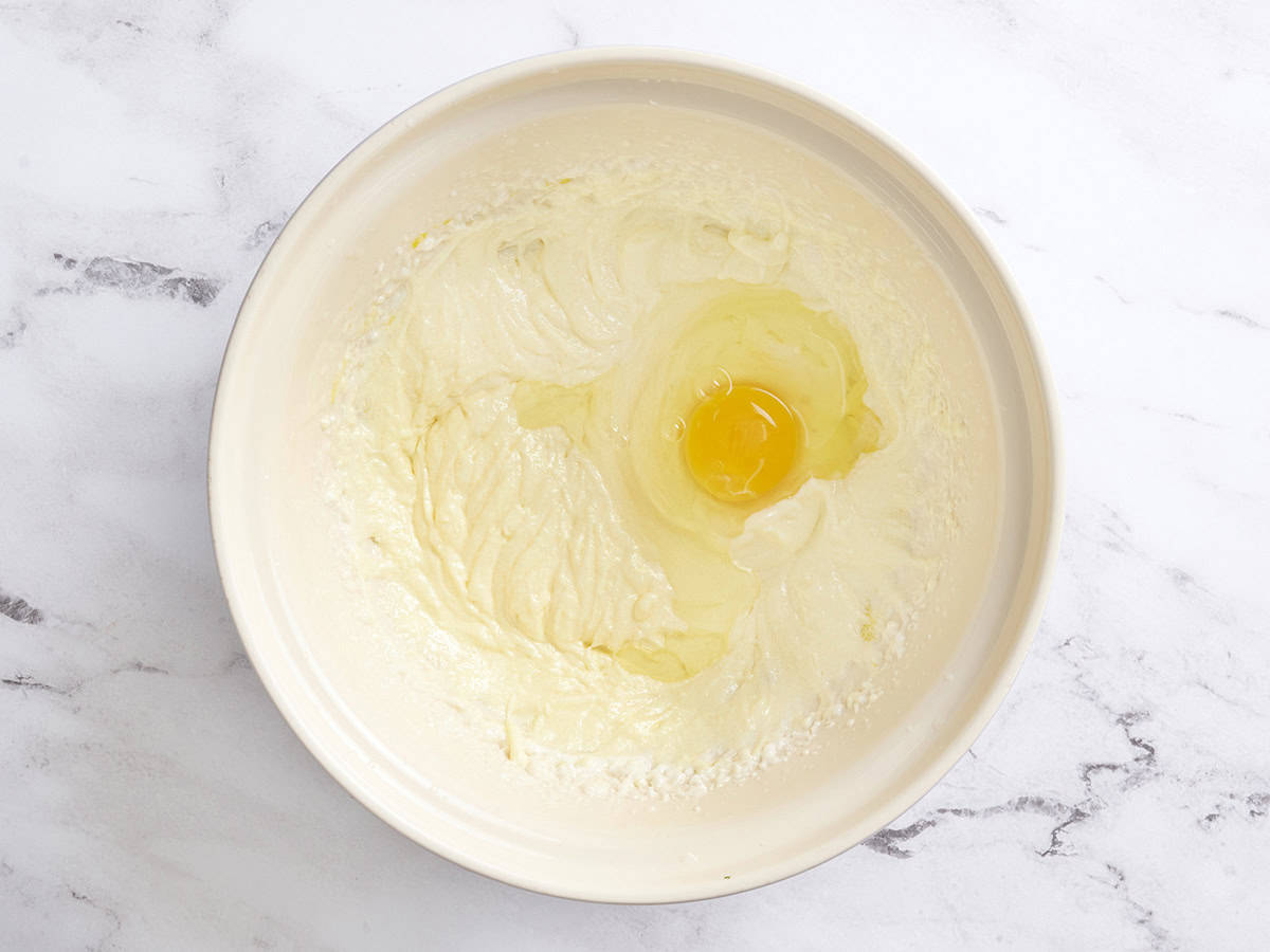 A egg added to beaten butter and sugar in a bowl.