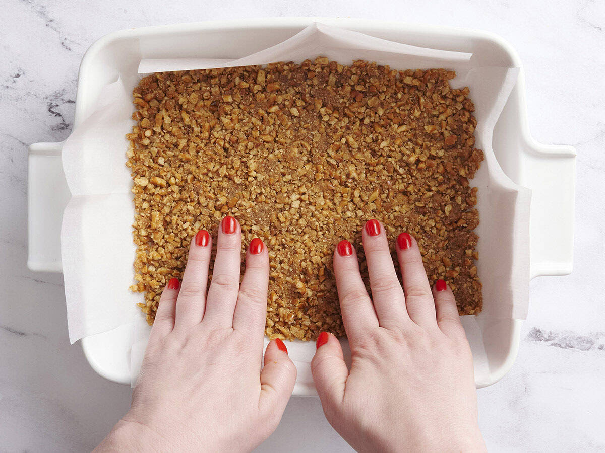 Crushed pretzels being pressed into a baking dish.