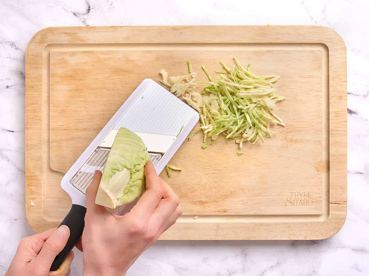 A hand using a mandoline slicer to slice green cabbage.