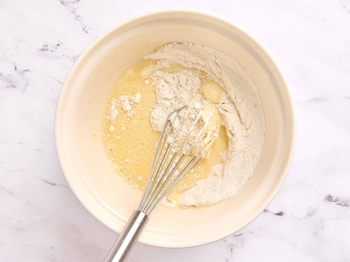A whisk combining the wet and dry ingredients for homemade pancakes in a bowl.