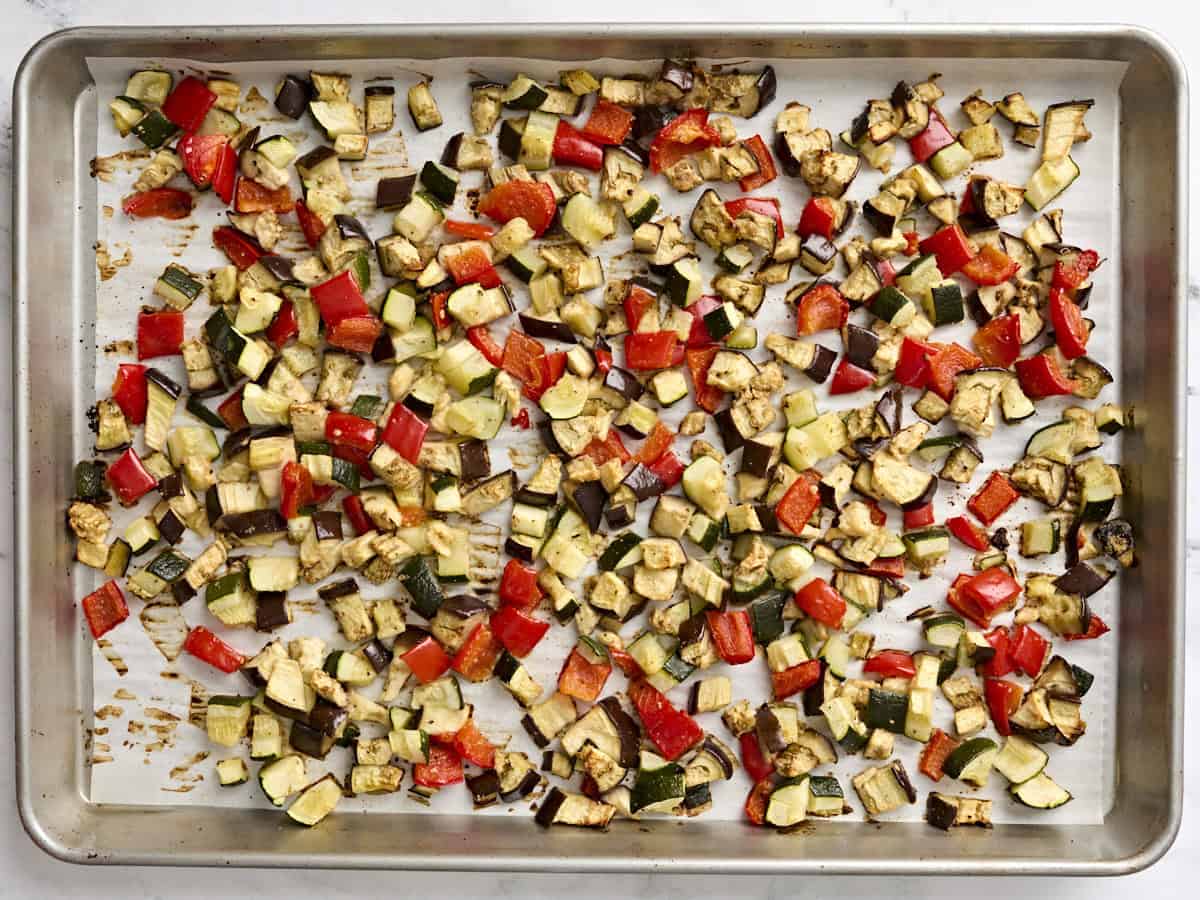 Roasted zucchini, eggplant, and red bell pepper on a parchment lined baking sheet.