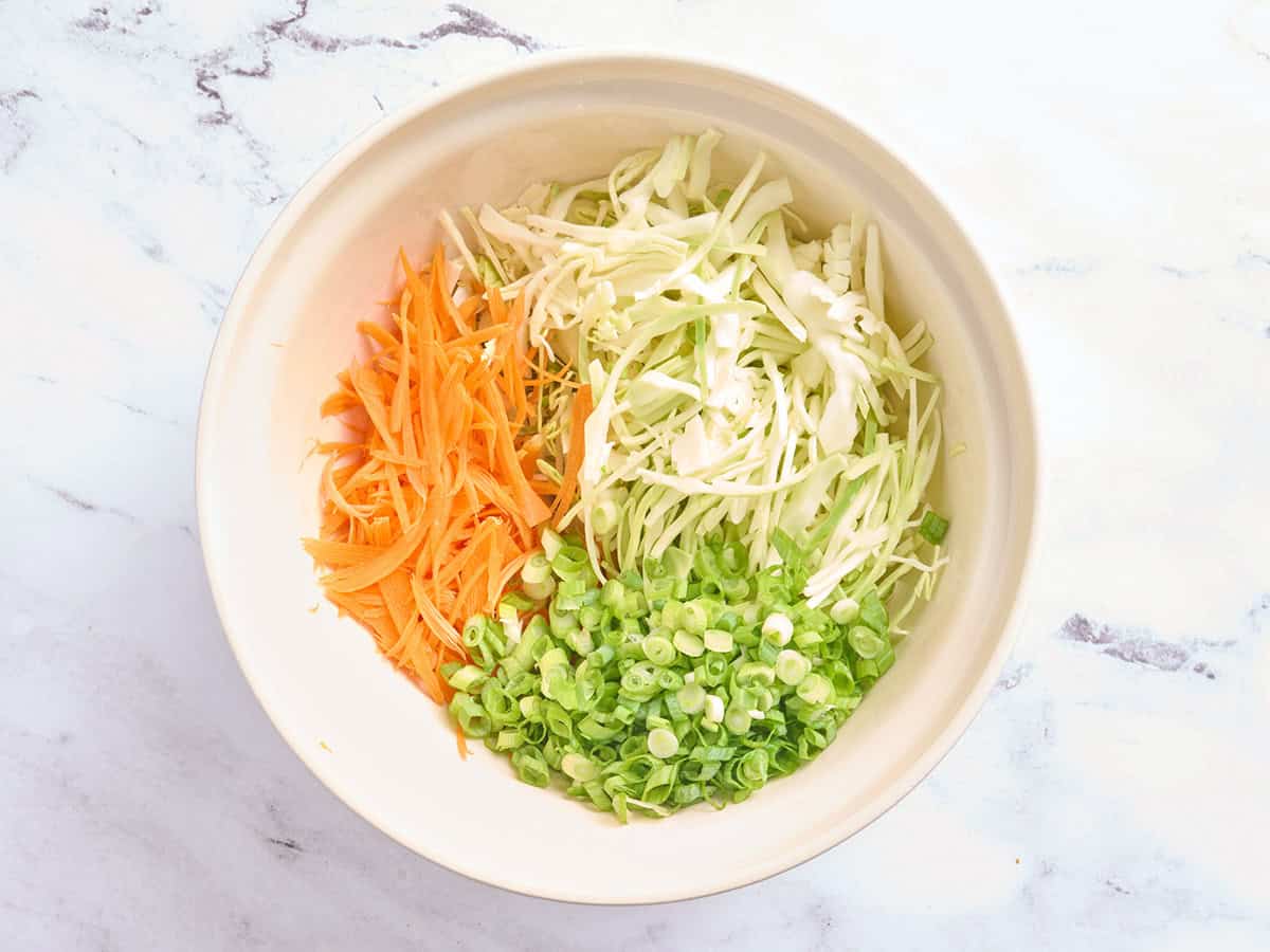 Shredded cabbage and carrot and sliced green onions in a bowl.