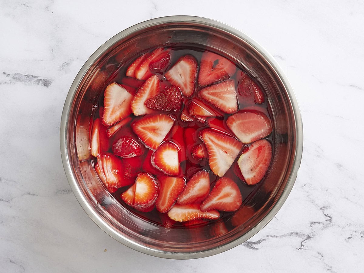 Sliced strawberries added to strawberry jello in a bowl.