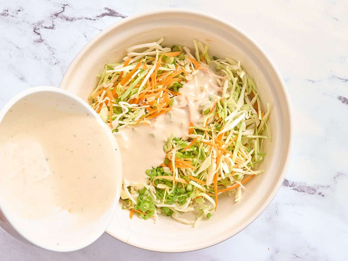 Coleslaw dressing being poured into the salad mix for coleslaw.