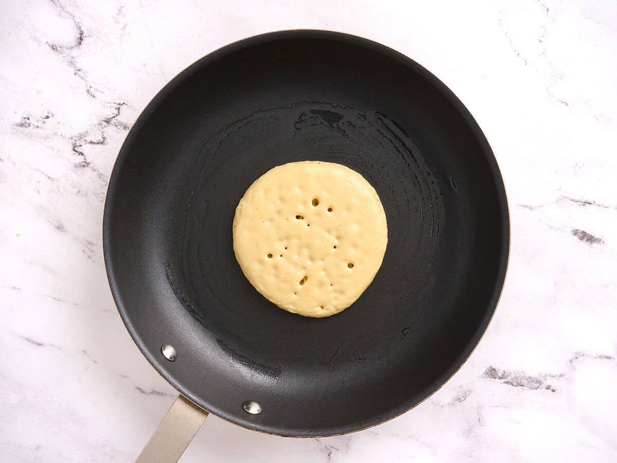 A pancake cooking in a skillet showing bubbles forming.