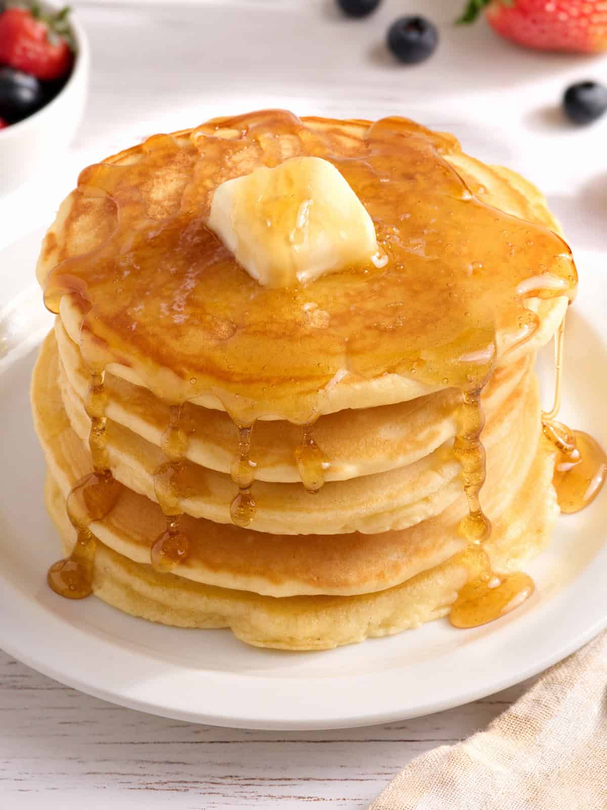Side view of a stack of homemade pancakes with butter and syrup.