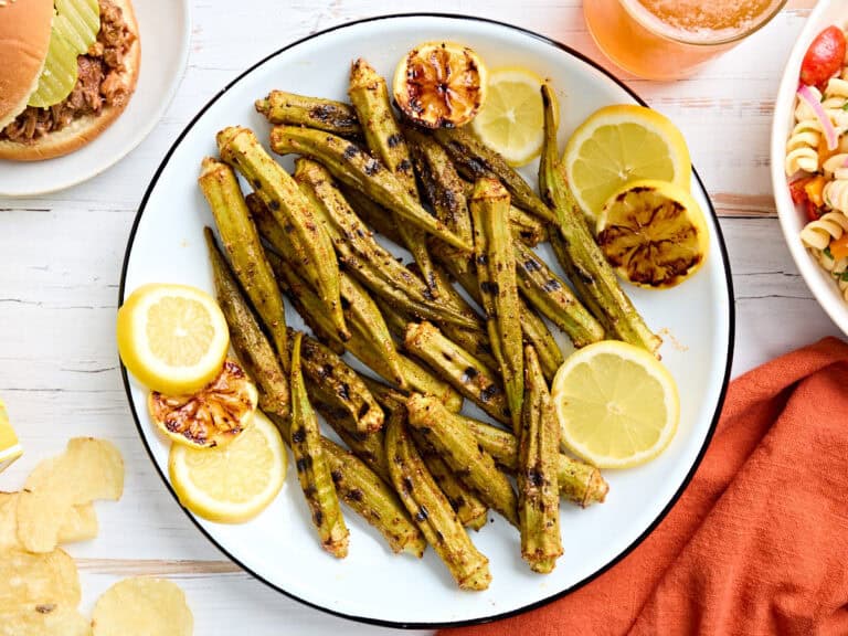 Overhead view of grilled okra on a plate with lemon slices.