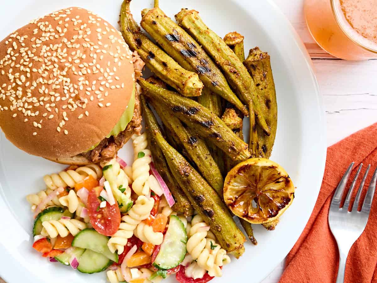 Gombo grilled on a plate with a hamburger and a salad of pasta.