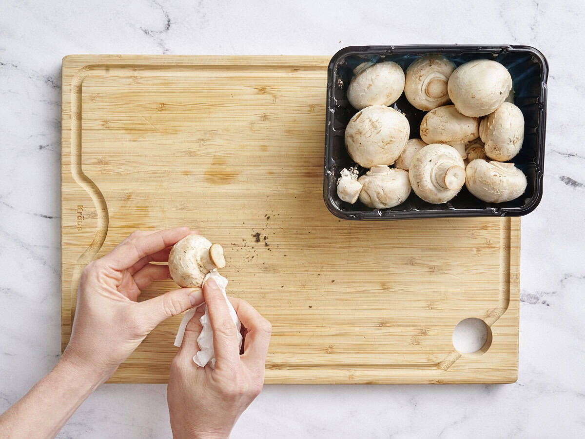 Hands using a paper towel to clean mushrooms.