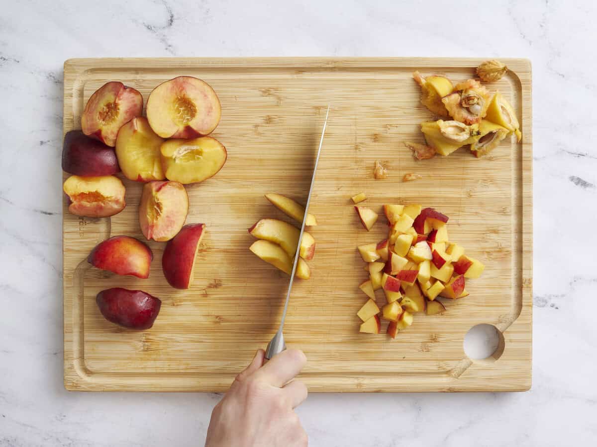 A knife dicing fresh peaches on a wooden cutting board.