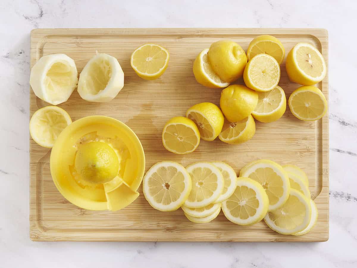 Lemons on a cutting board with some being juice and the other cut into round.
