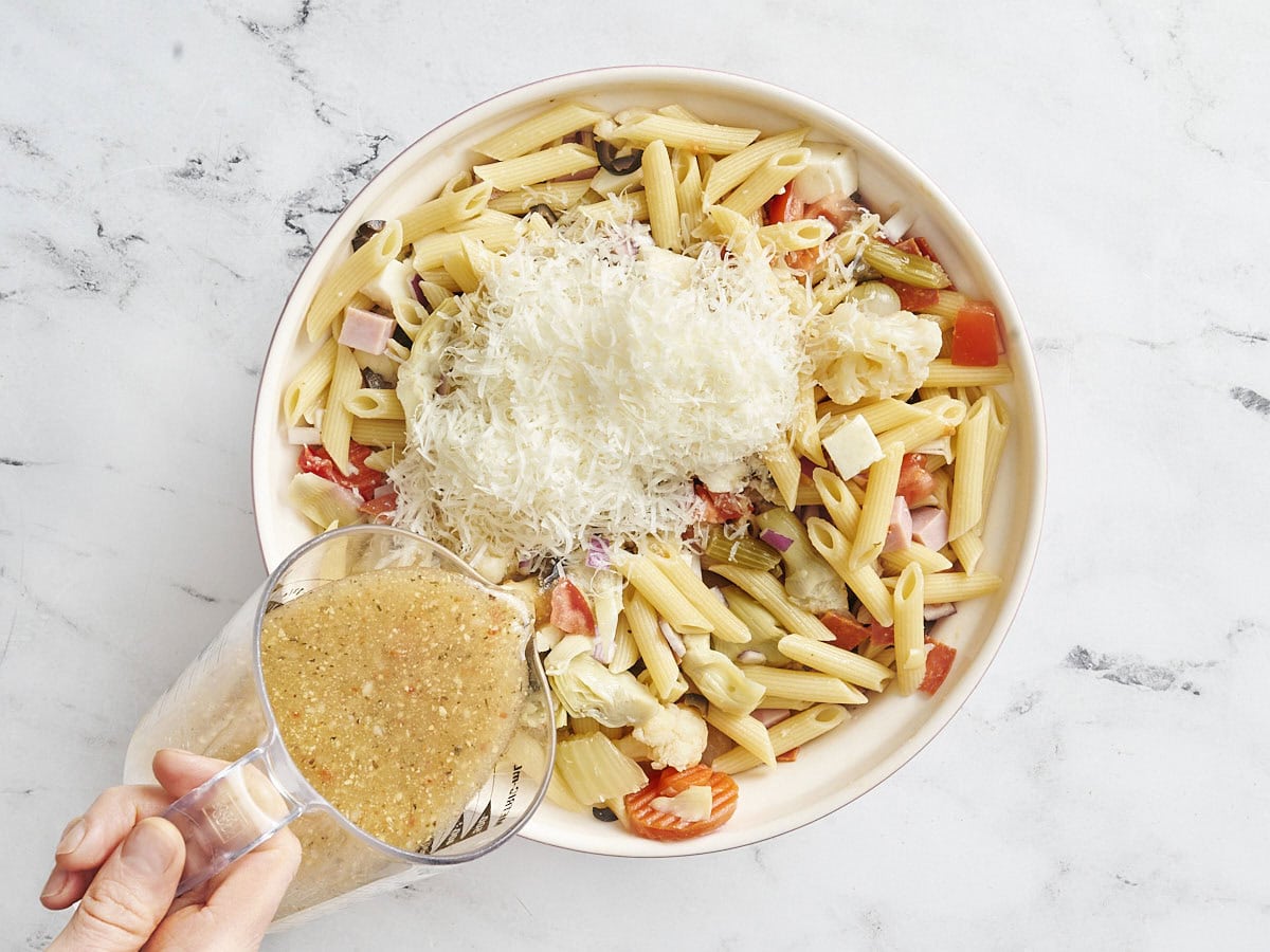 Shredded parmesan and italian dressing added to antipasto salad in a bowl.