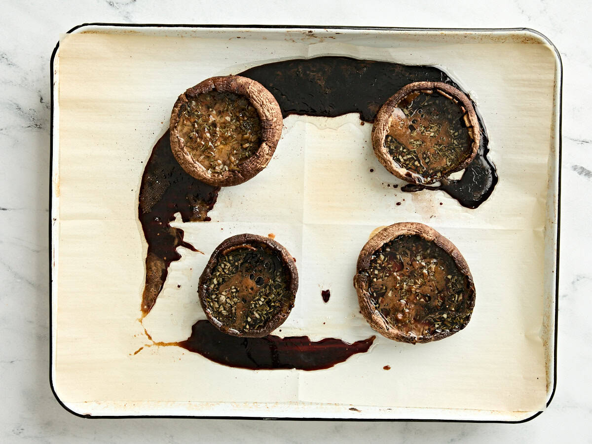 Four baked portabella mushrooms on a parchment lined baking sheet.