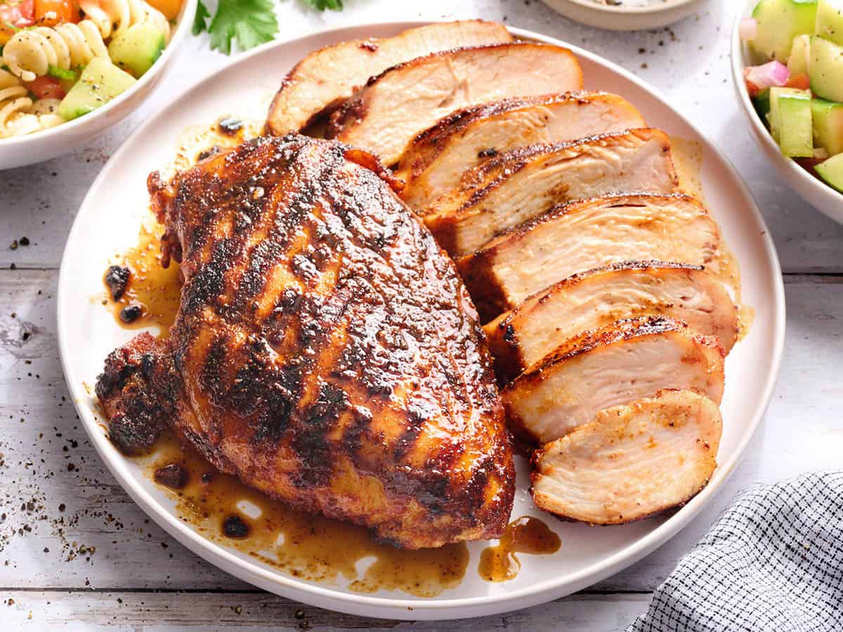 Side view of a grilled chicken breast on a plate with another breast cut into slices.