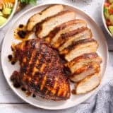 Overhead view of a grilled chicken breast on a plate with another breast cut into slices.