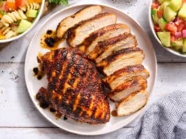 Overhead view of a grilled chicken breast on a plate with another breast cut into slices.