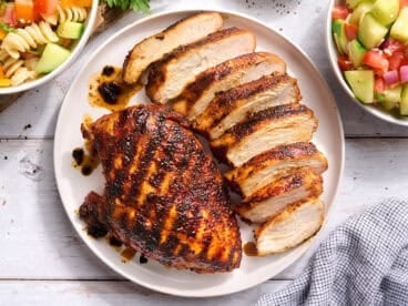 Overhead view of a grilled chicken breast on a plate with another breast cut into slices.