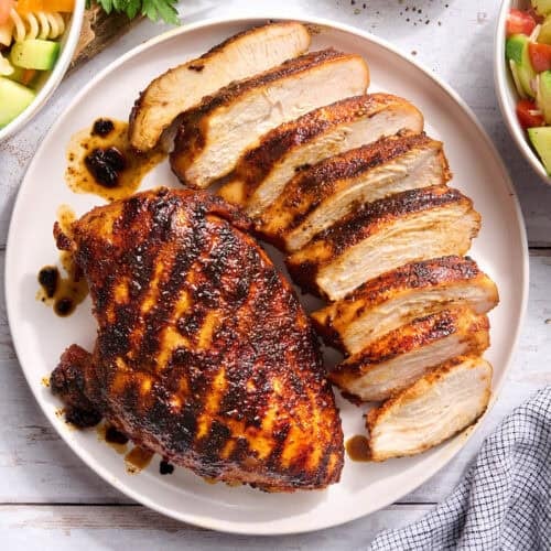 Overhead view of a grilled chicken breast on a plate with another breast cut into slices.