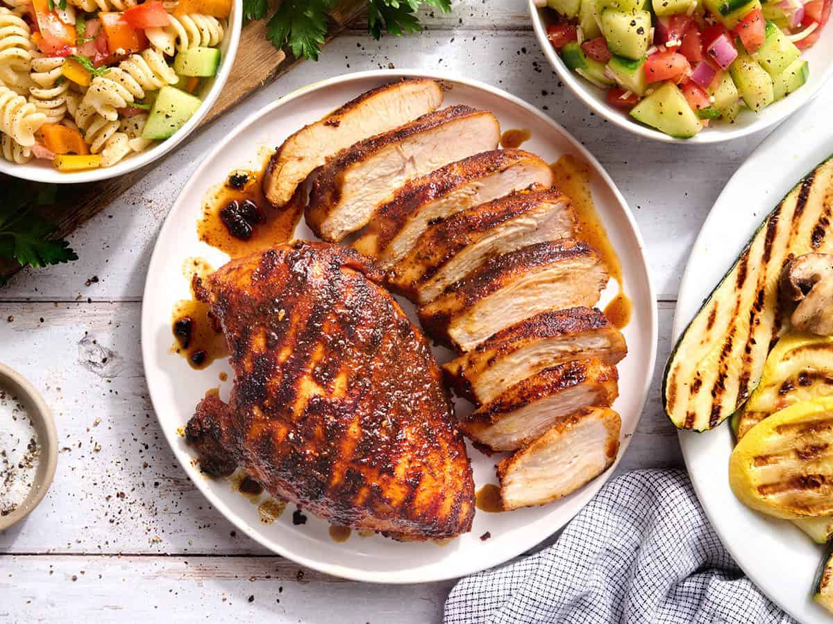Overhead view of a grilled chicken breast on a plate with another breast cut into slices.