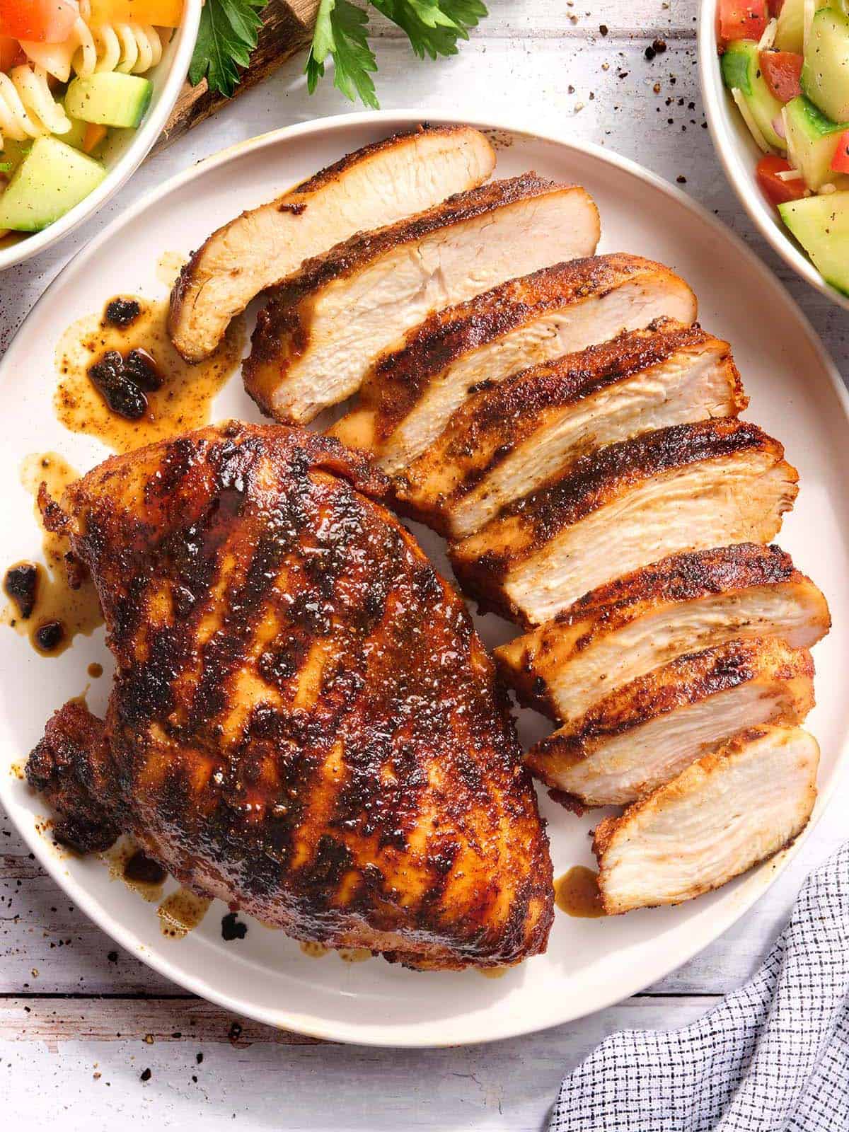 Overhead view of a grilled chicken breast on a plate with another breast cut into slices.
