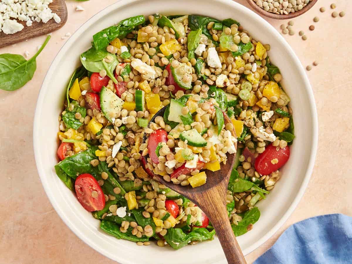 Overhead view of a bowl of summer lentil salad with a wooden spoon taking some.
