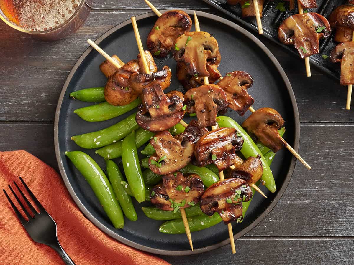 Overhead view of grilled mushroom kebabs on a plate with  sugar snap peas.
