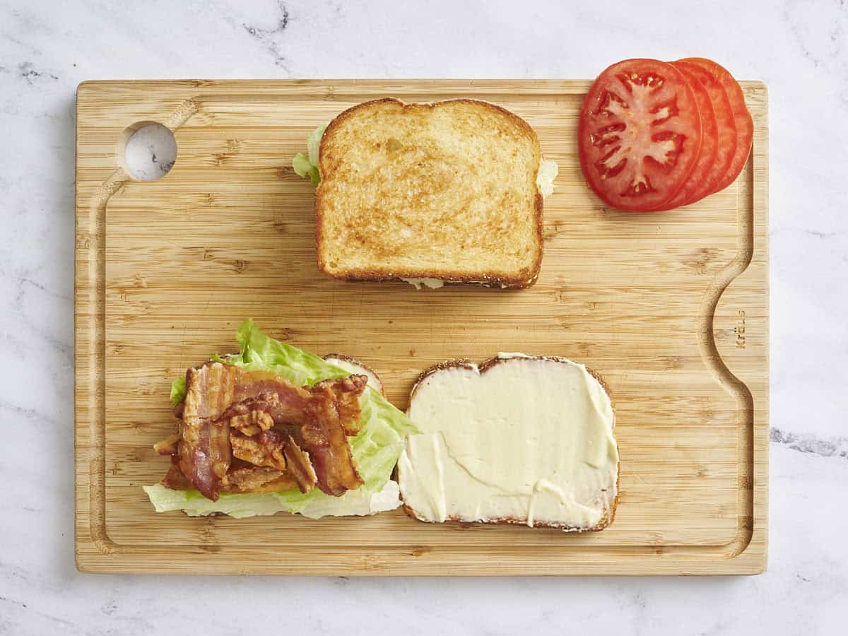 Overhead view of two BLT sandwiches, with one open showing the lettuce and bacon with sliced tomatoes placed to the side.