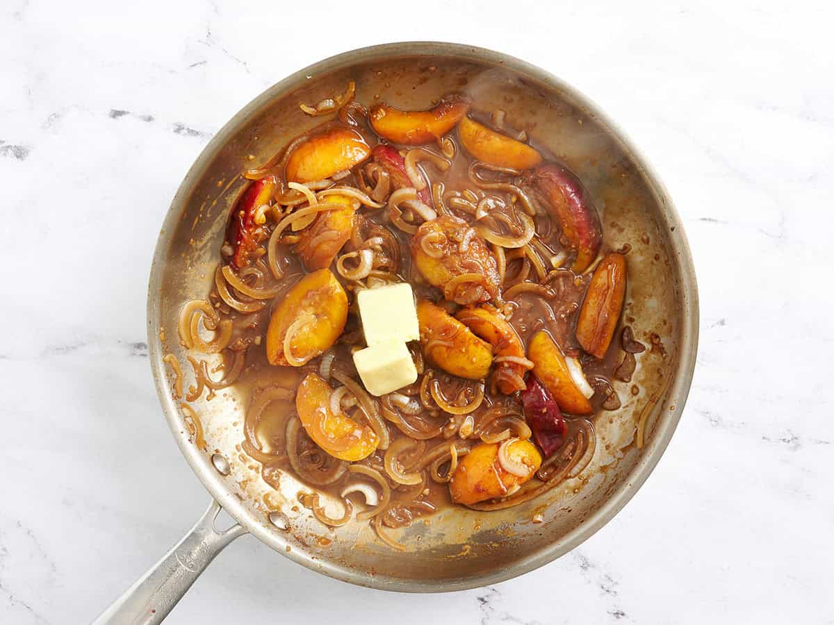 Butter added to a peach and onion sauce in a skillet.
