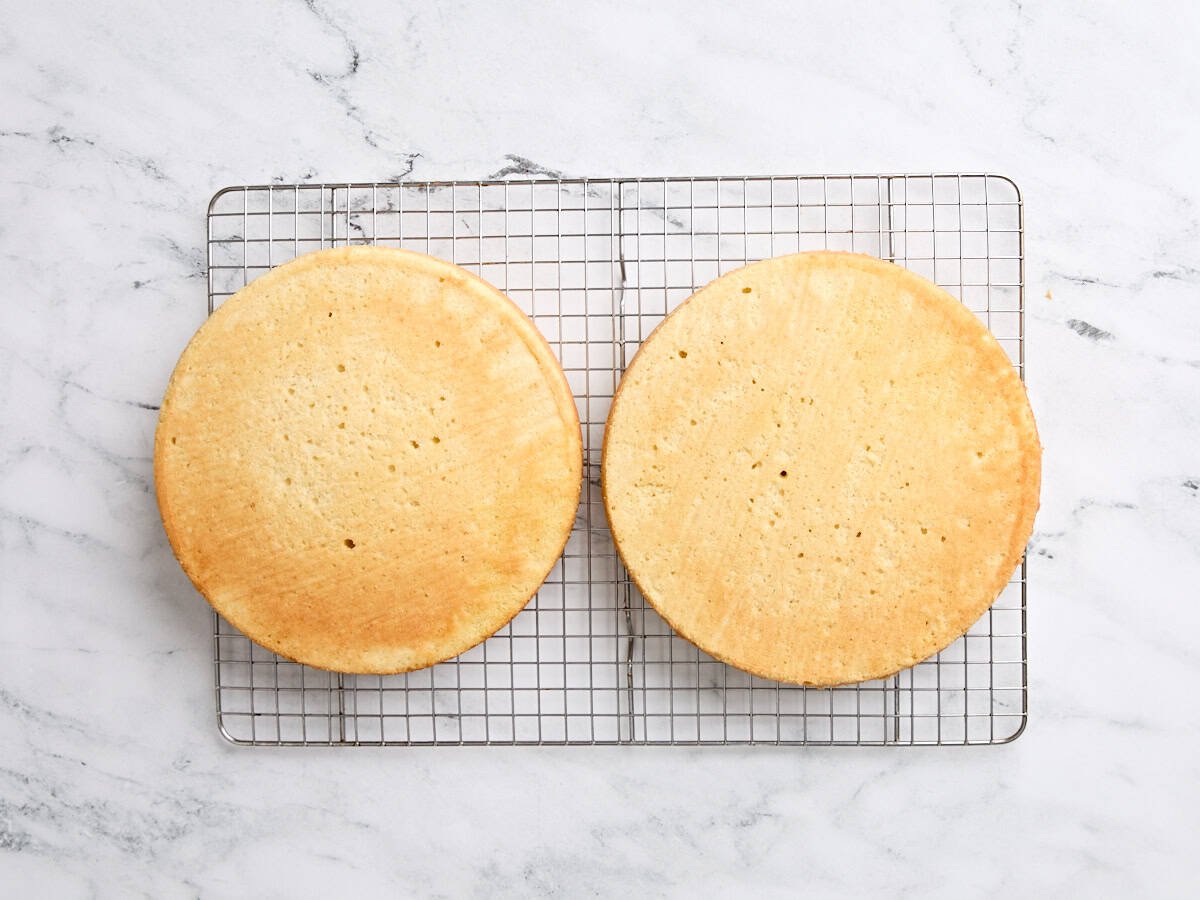 Two vanilla cakes cooling on a cooling rack.