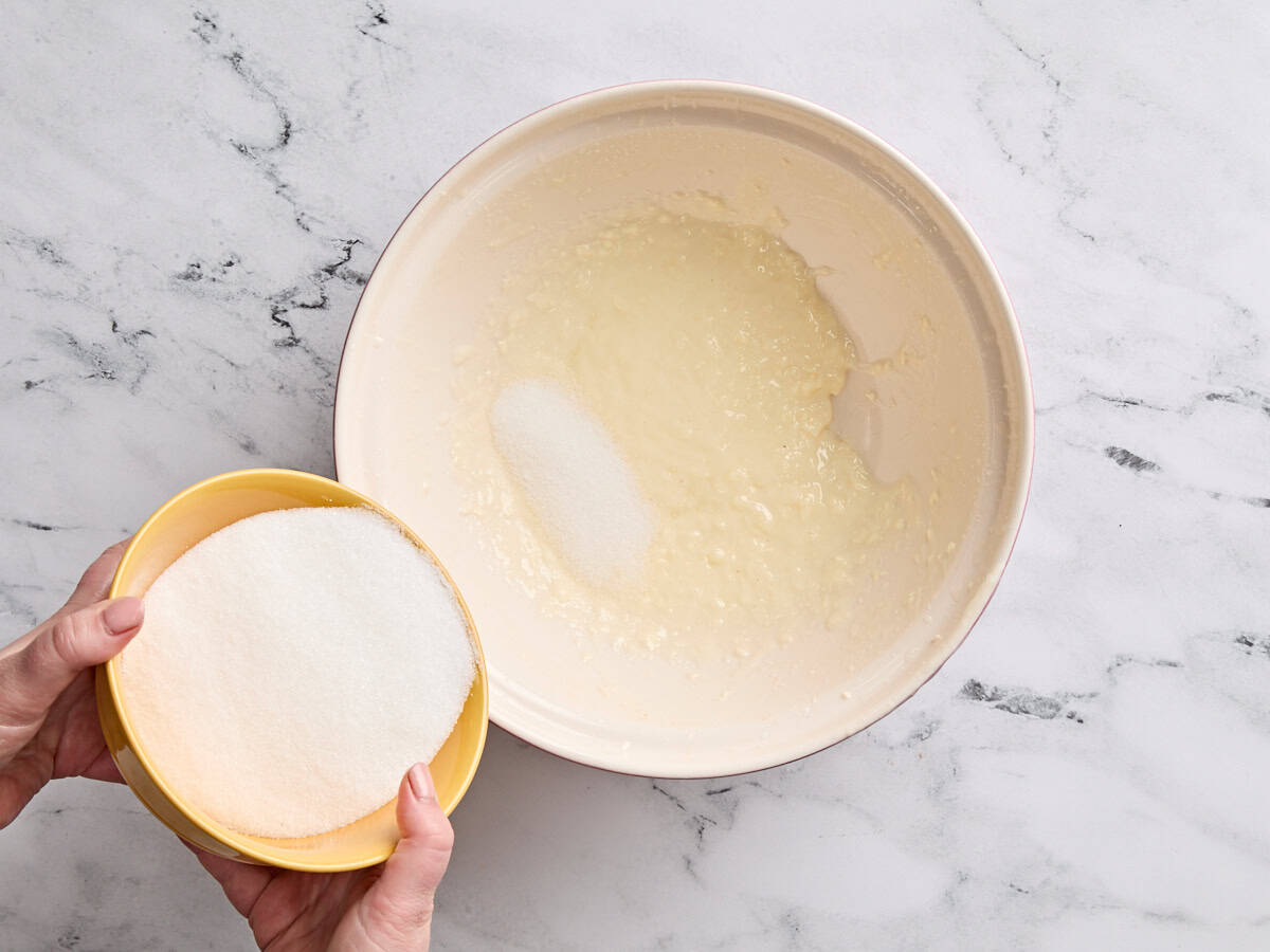 Sugar being poured into beaten butter and oil.
