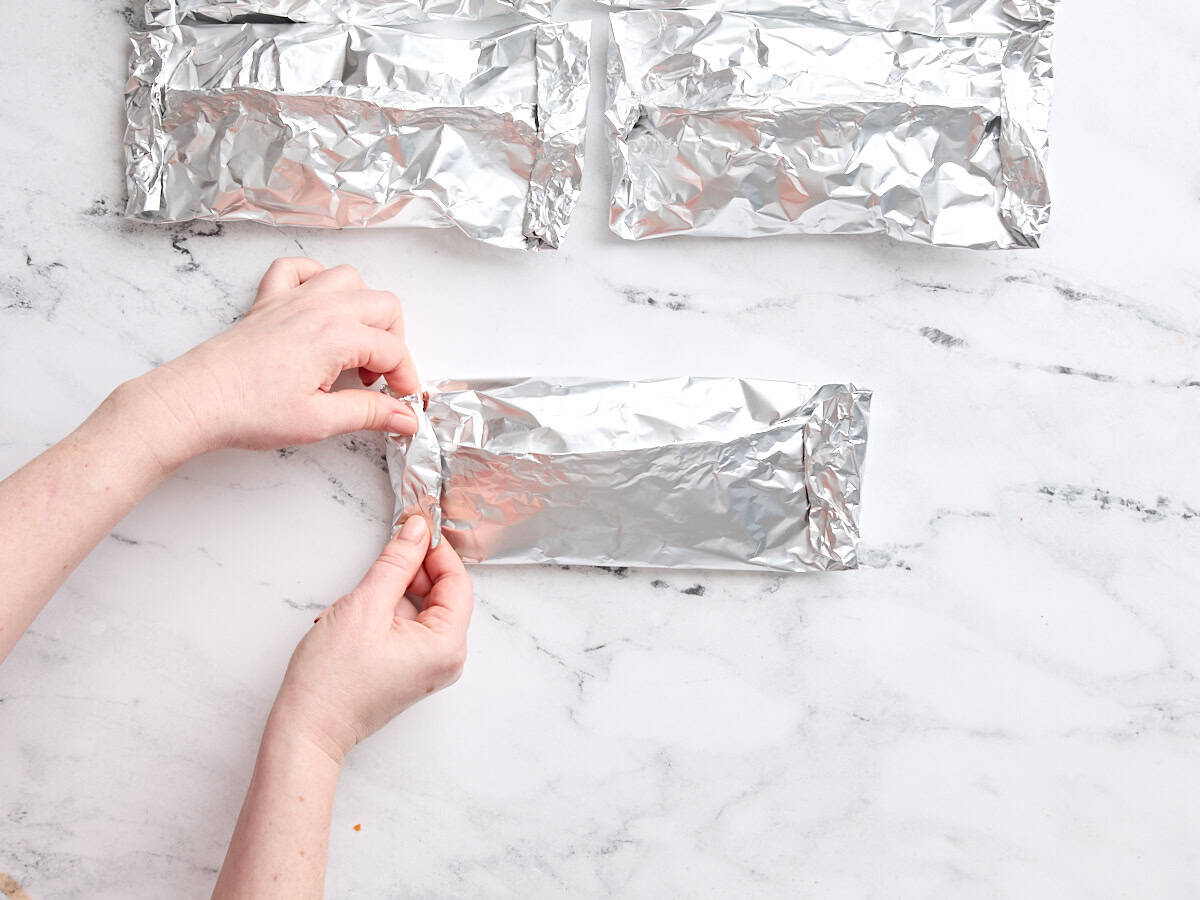 Hands sealing the edges of a shrimp and vegetable foil packet.
