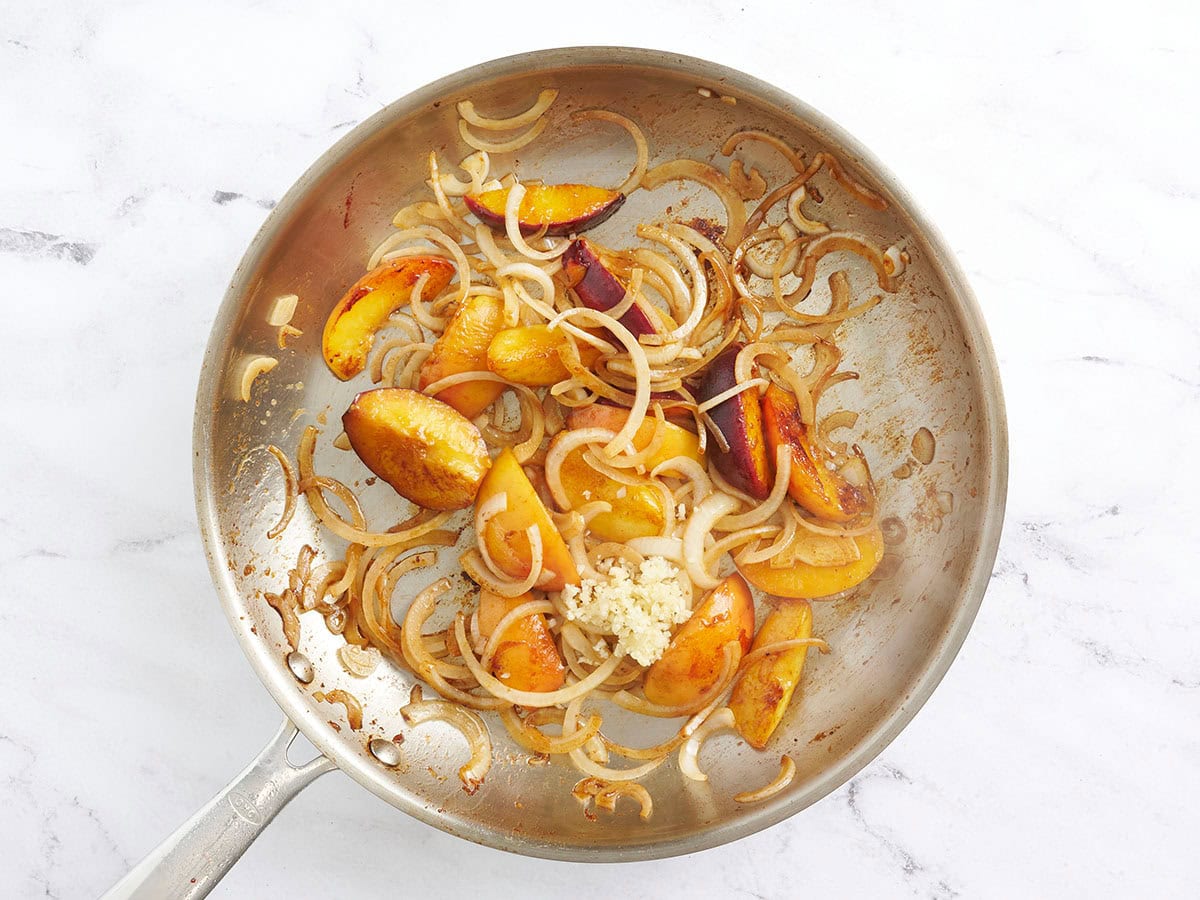 Sauteed peach slices and onions in a skillet with minced garlic.