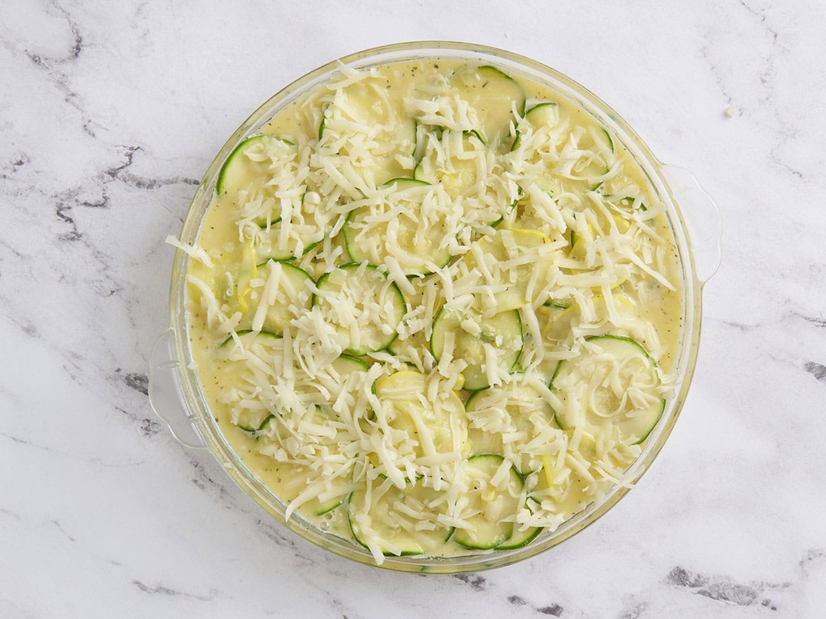 The ingredients for zucchini and corn pie in a skillet topped with shredded cheese.