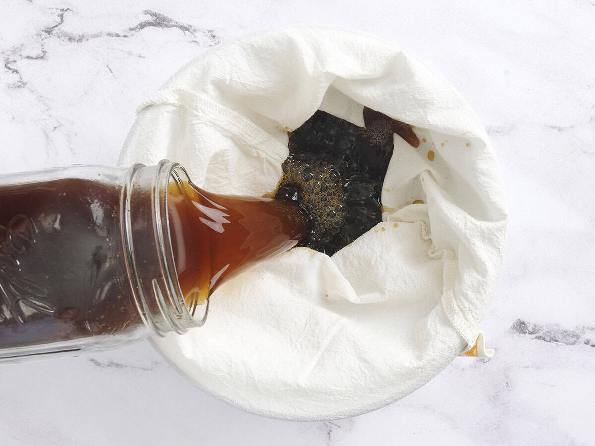 Cold brew coffee being poured into a nut milk bag into a bowl.