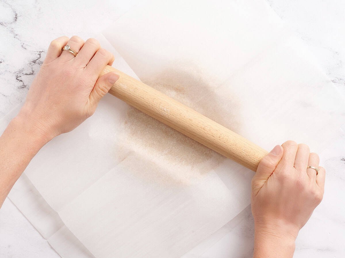 Cookie dough being rolled between two sheets of parchment paper.