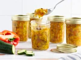 Side view of jars of zucchini relish, is a spoon taking some from one jar.