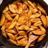 Overhead view of a skillet of fried apples with a wooden spoon stirring them.
