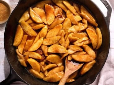 Overhead view of a skillet of fried apples with a wooden spoon stirring them.