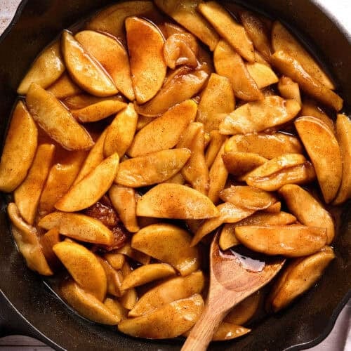 Overhead view of a skillet of fried apples with a wooden spoon stirring them.