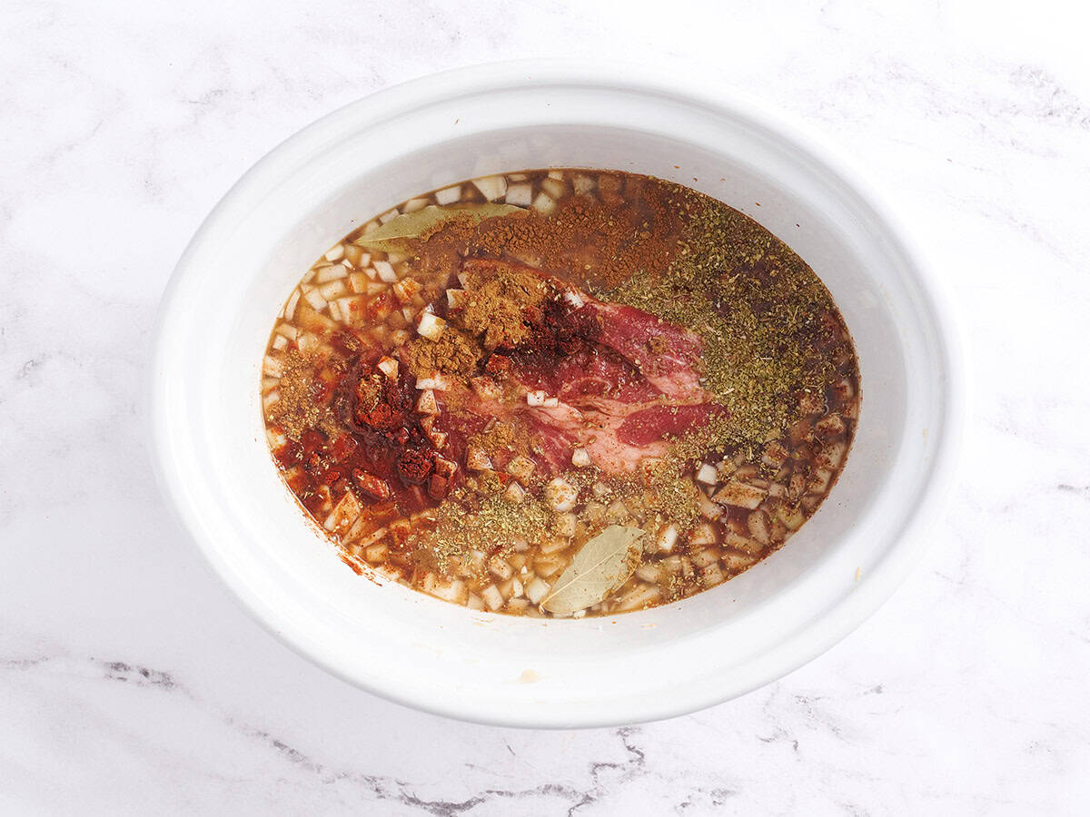 A chuck roast with seasonings in a crockpot.