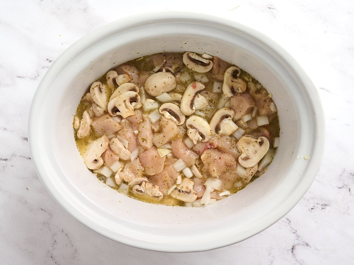 Raw diced chicken breasts and sliced mushrooms in a crockpot before cooking.