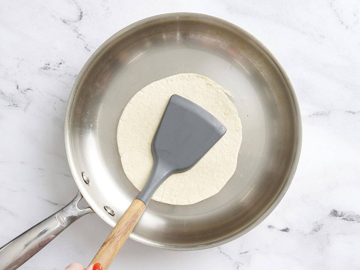 A spatula pressing down a tortilla in a skillet.