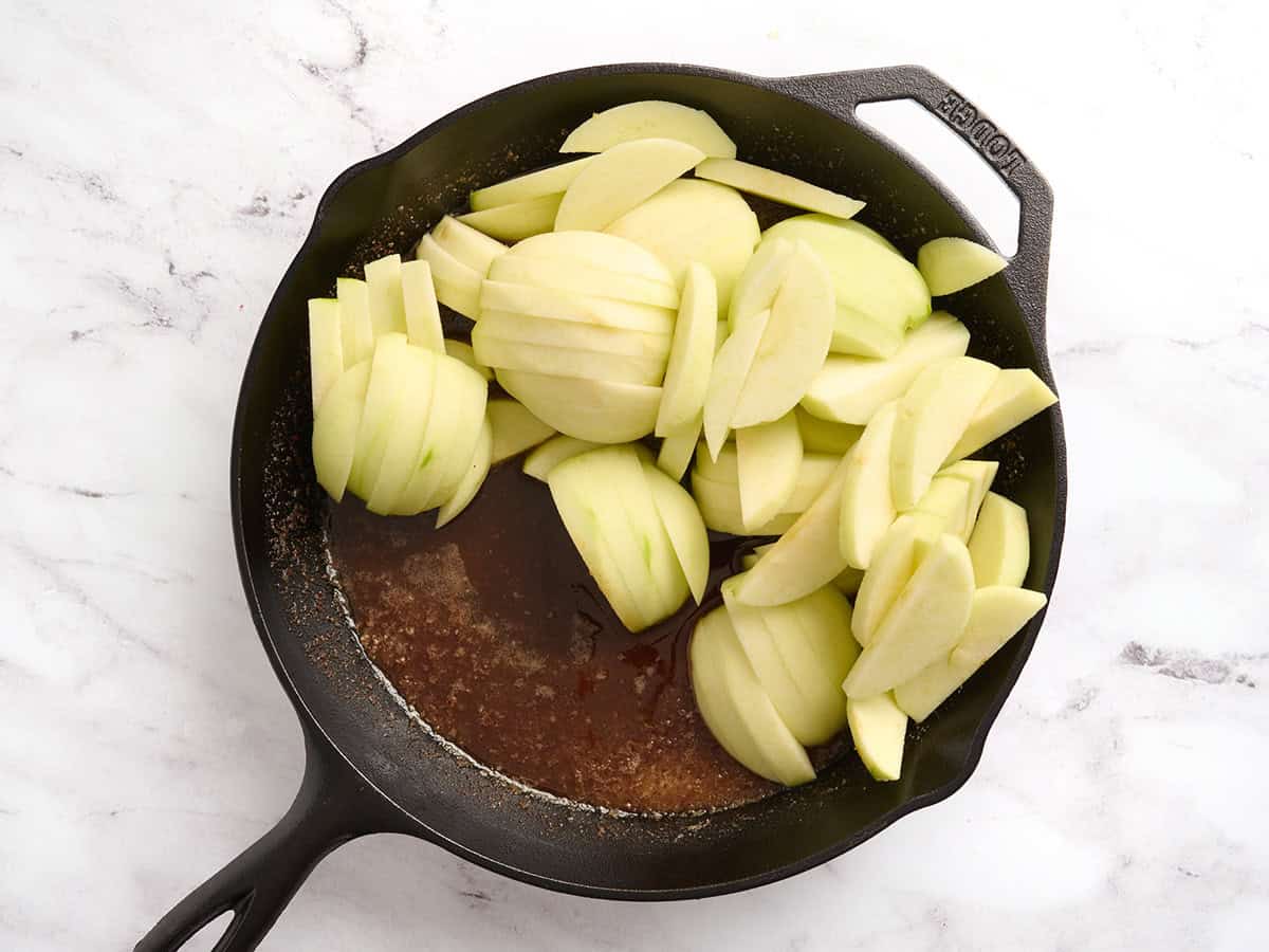 Sliced and peeled apples added to a skillet with seasonings and sugar.
