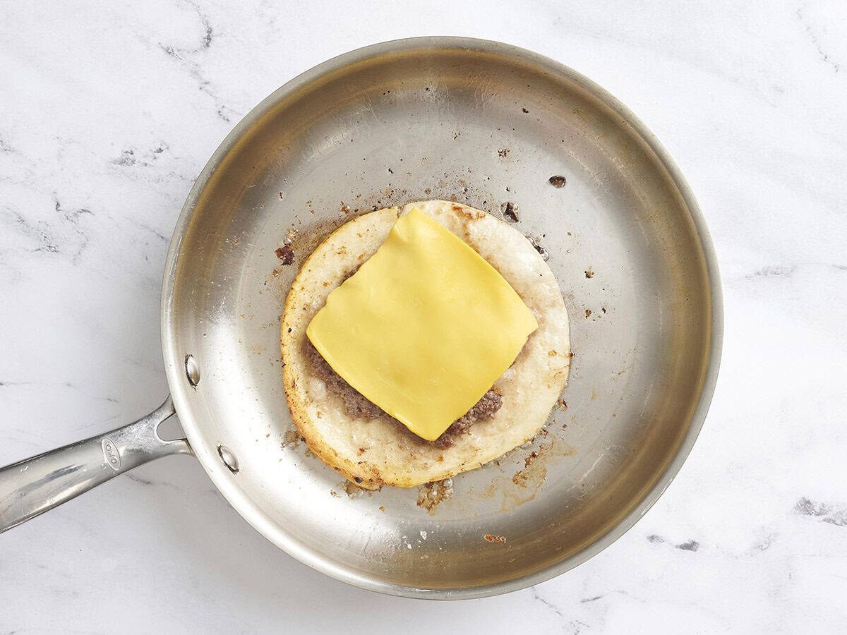 A smash burger taco in a skillet topped with a slice of American cheese.